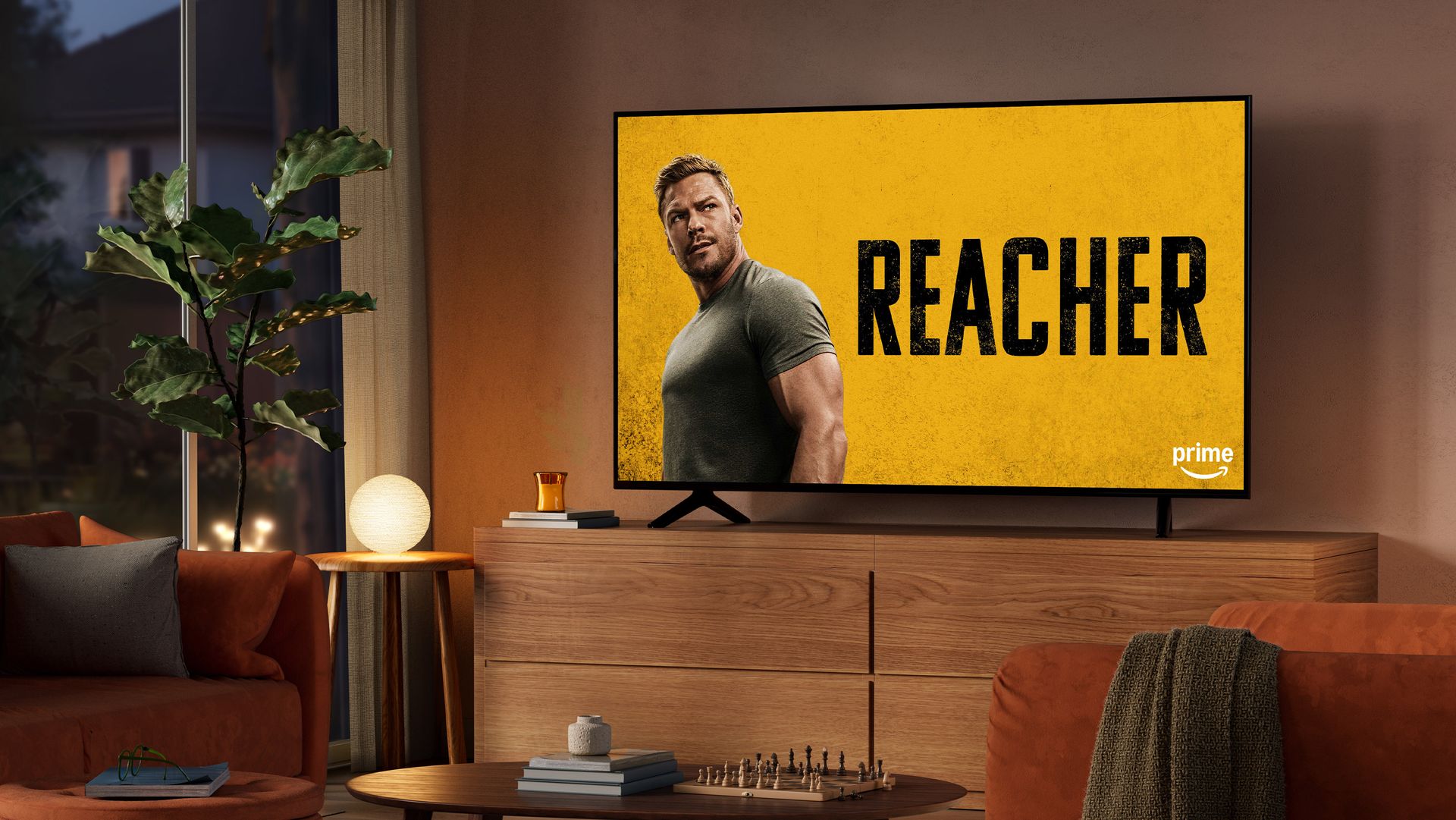 A dimly lit living room at night with the TV on an entertainment console. Reacher is on screen.