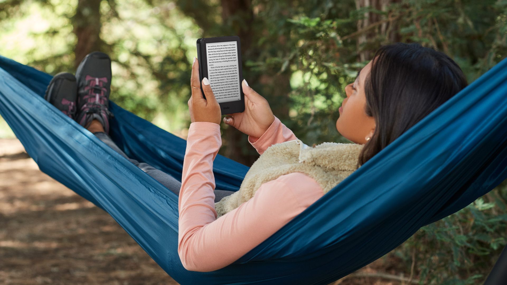 Woman reading on a Kindle while lying in a hammock outside